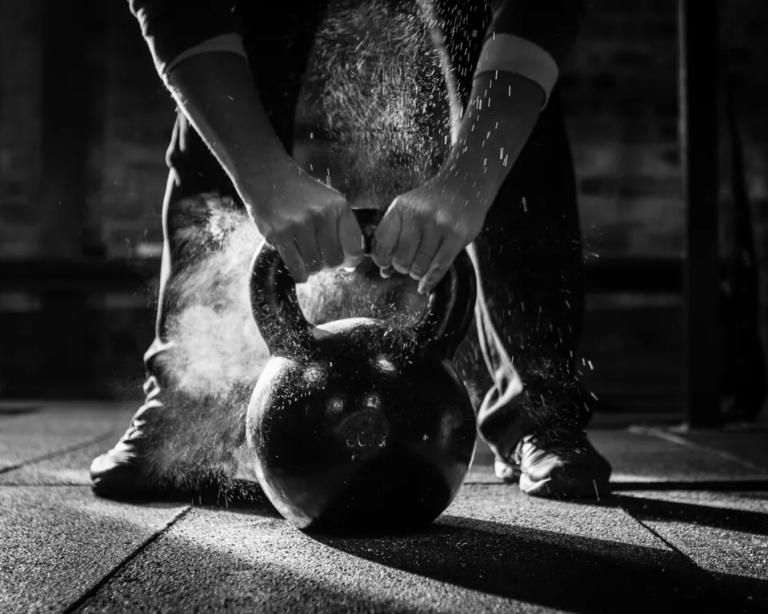 Athlete using chalk for a heavy kettlebell lift to build strength and energy with AlphaGenics TRT
